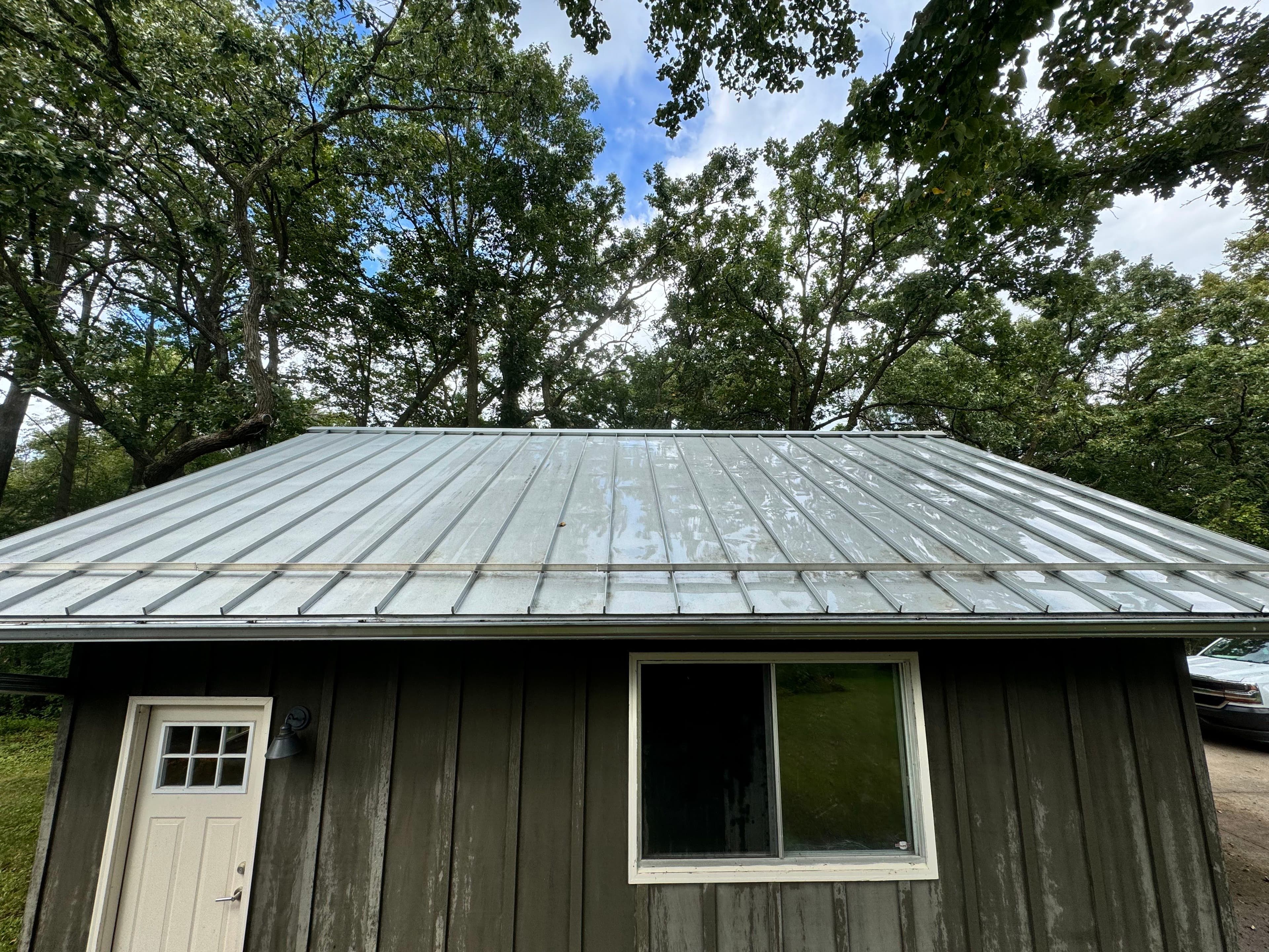 Metal roof cabin surrounded by trees under a clear blue sky. Ideal for nature retreats.