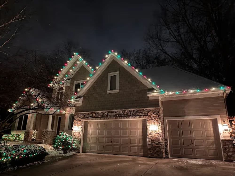 Festively decorated house at night with colorful Christmas lights and a snowy landscape.