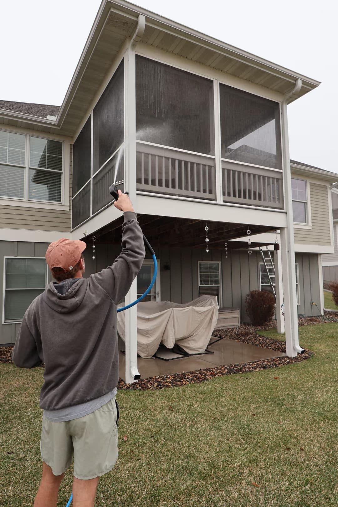 Person cleaning outdoor screened porch with a spray nozzle, house in background.