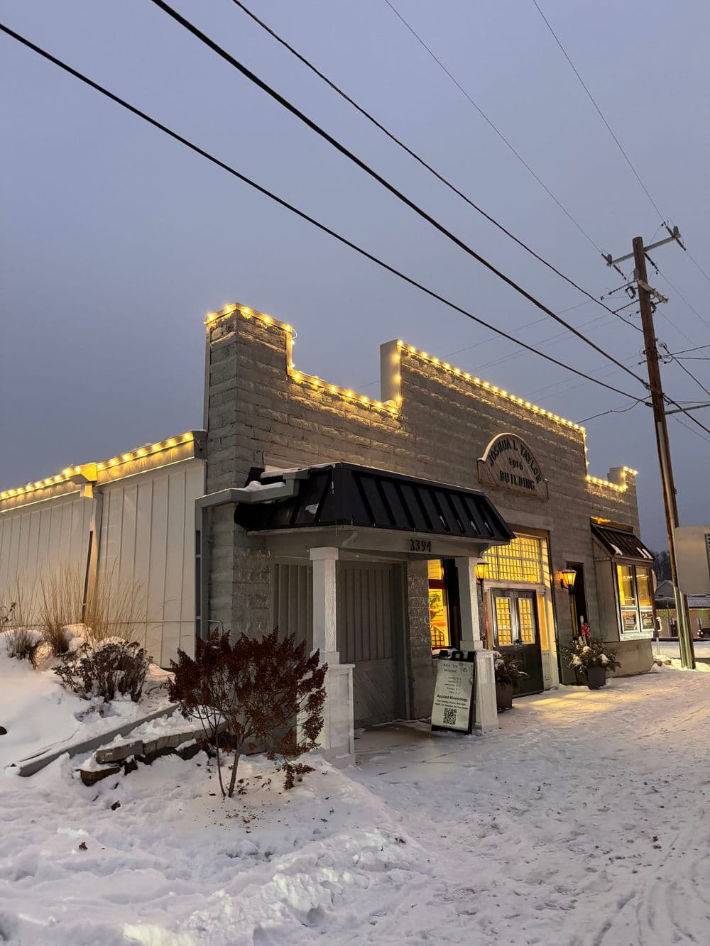 Snow-covered restaurant facade decorated with warm lights at dusk. 3396 location.