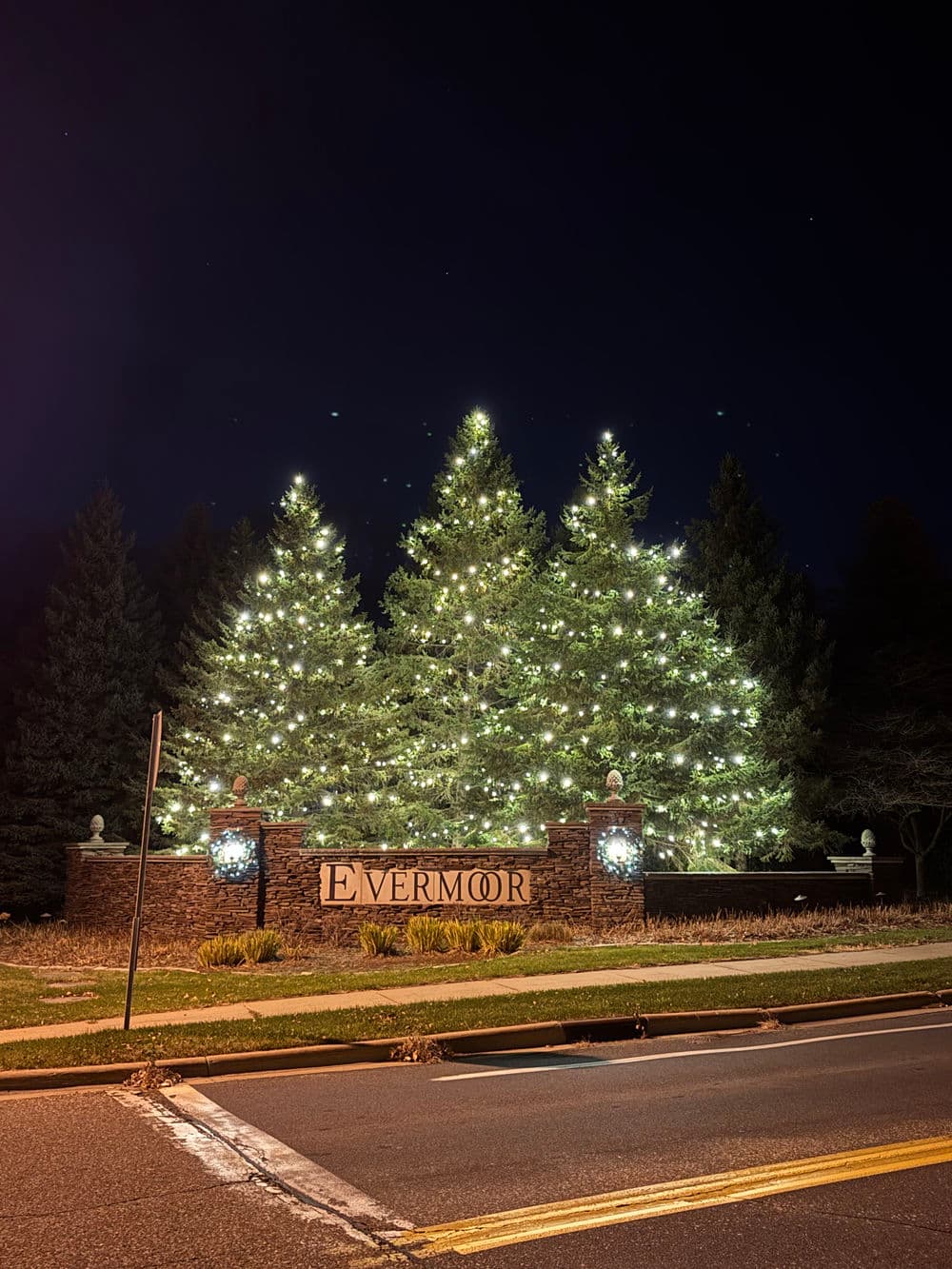 Evermoor entrance sign surrounded by illuminated trees at night.