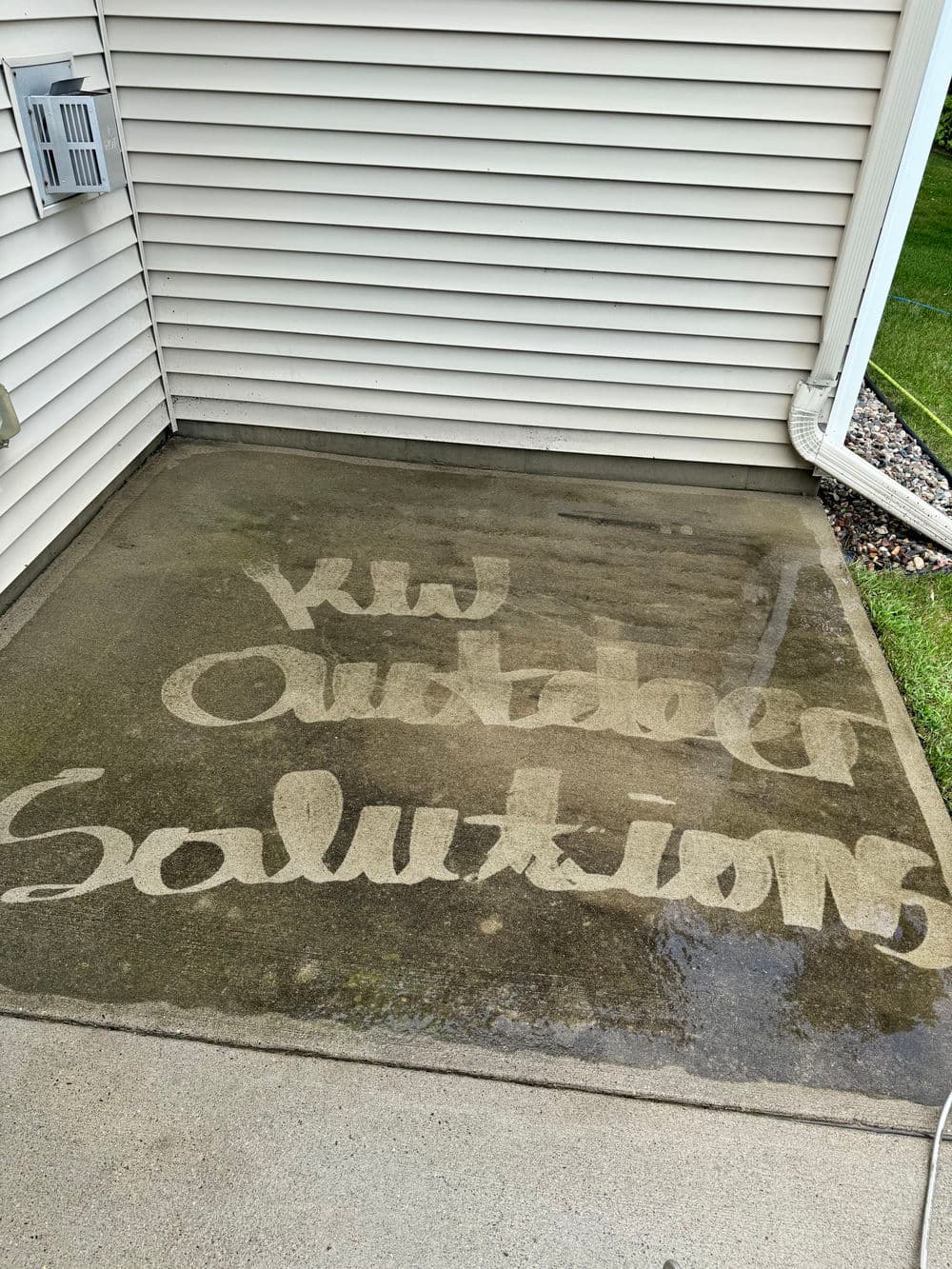 KW Outdoor Solutions logo written on wet concrete surface outside a house.