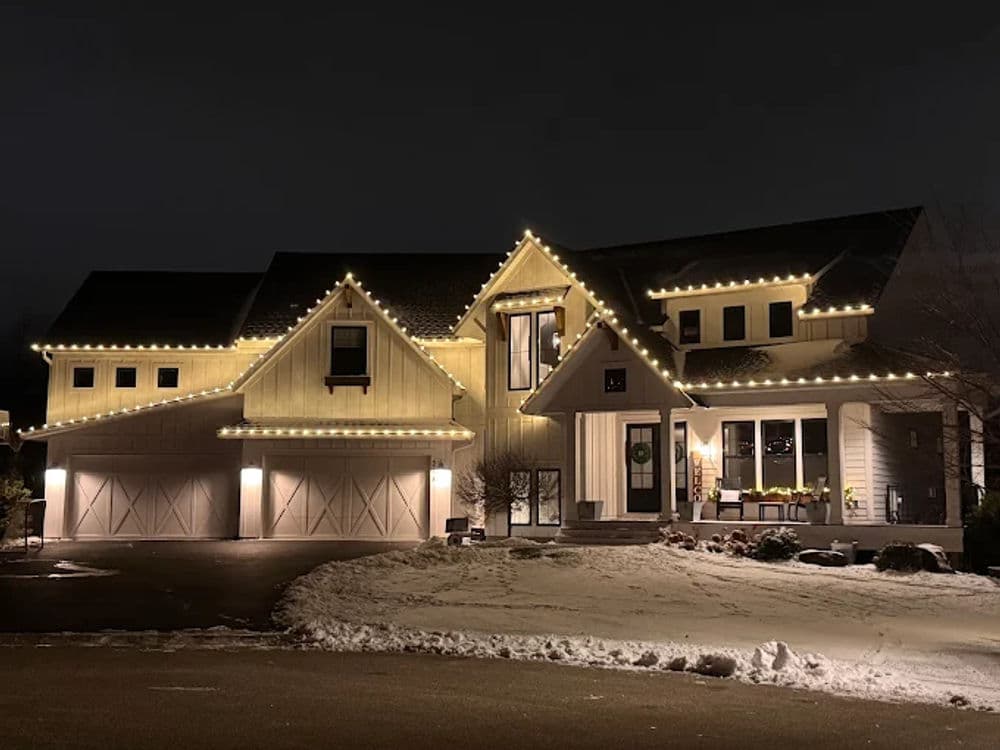 Elegant modern home adorned with festive holiday lights in a snowy winter landscape.