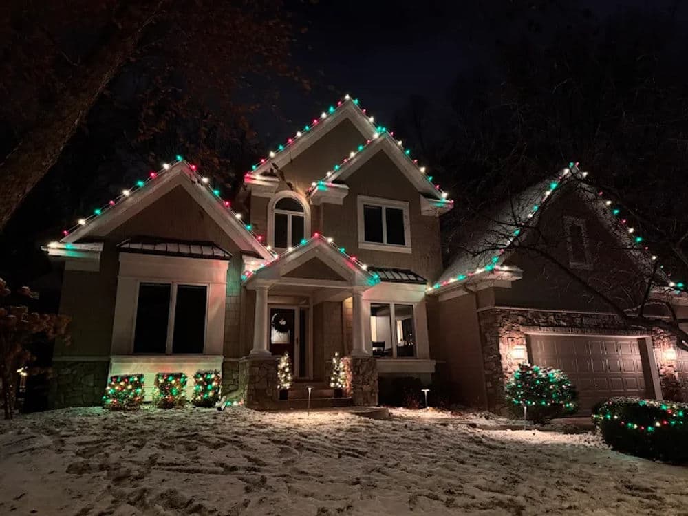 Festively decorated house with colorful lights and snow during winter night.