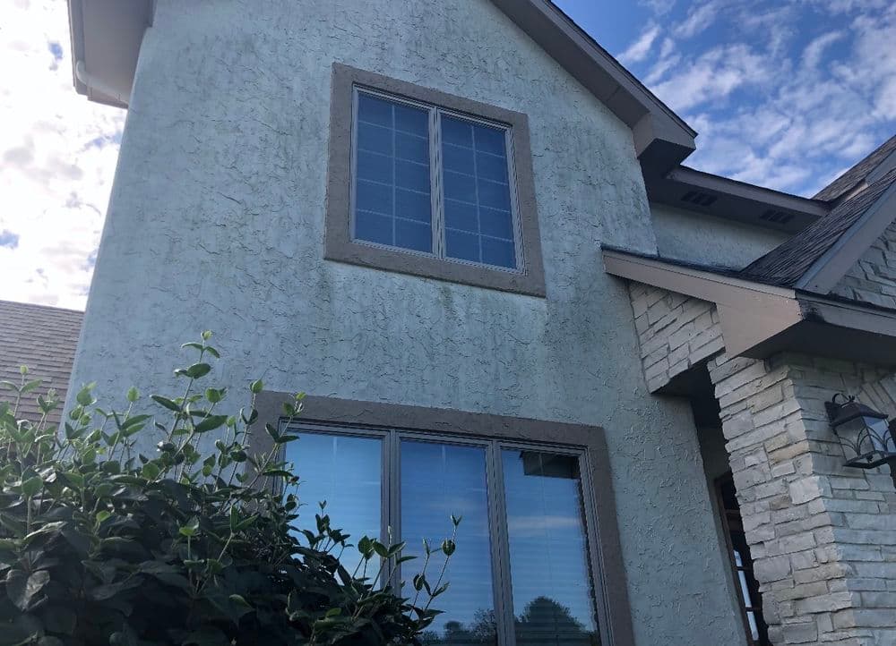Close-up of a textured house exterior with windows and a blue sky background.