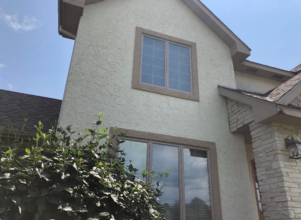 Residential home exterior with textured stucco finish and large window surrounded by greenery.